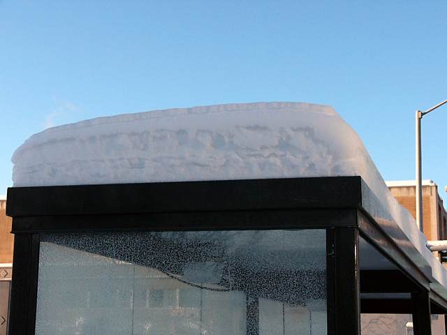 A closer look at the snow piled atop the bus shelter.