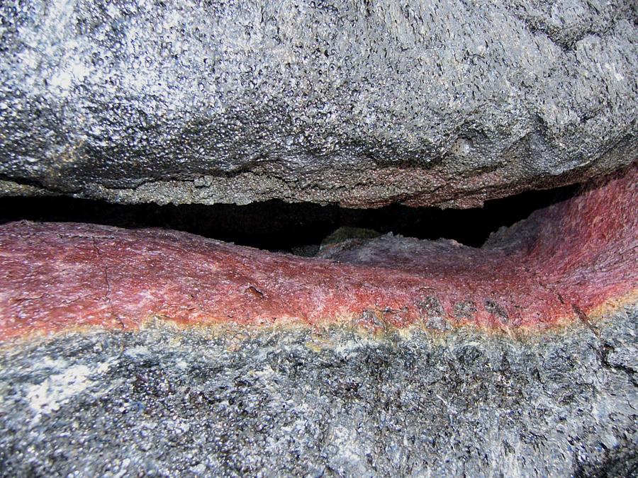 A small fissure in the lava reveals red colored rock